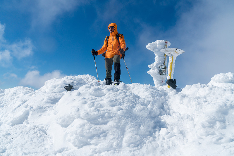 一位登山运动员在白雪皑皑的山顶上穿着亮橙色的软壳夹克。积极的人概念形象的Velky Krivan，斯