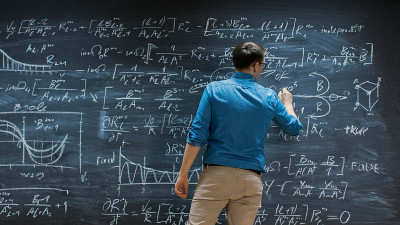 聪明的年轻数学家正在大黑板上写和思考解决长和复杂的方程/公式。