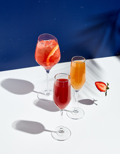 白色桌子，蓝色背景，Aperol饮料和贝里尼鸡尾酒。阳光和棕榈叶影饮现代静物。夏天，派对，热带和新鲜