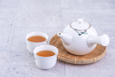 白茶壶和筛子上的茶杯里放着热茶，背景是亮灰色的水泥。