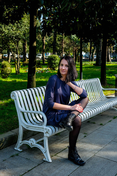 漂亮的黑发女人穿着裙子坐在街上的白色长凳上。享受阳光明媚的春日。