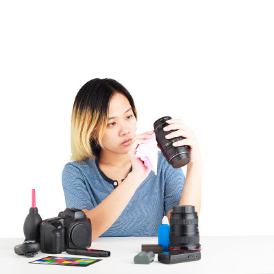 一名亚洲妇女正在用桌布和桌子上的摄影器材清洁照相机。对象隔离在白色背景与剪切路径和复制空间。