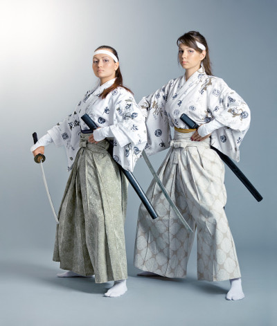 两个年轻的女人在日本服装与武士刀摆姿势
