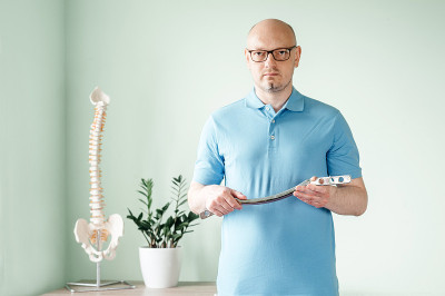 一名男性整骨医师，手持用于软组织治疗的不锈钢IASTM治疗工具，工具辅助软组织移动和最终筋膜松解