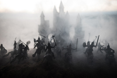 有骑兵和步兵的中世纪战斗场景。剪影的人物作为单独的对象，战斗之间的战士在日落雾蒙蒙的背景。