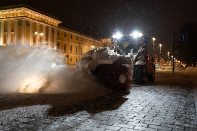 黄色的拖拉机和旋转清扫车在冬天的夜晚清理城市的街道。除雪设备