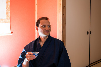 传统的日本町屋客栈与男子在和服的凹室和挂纸卷轴喝绿茶