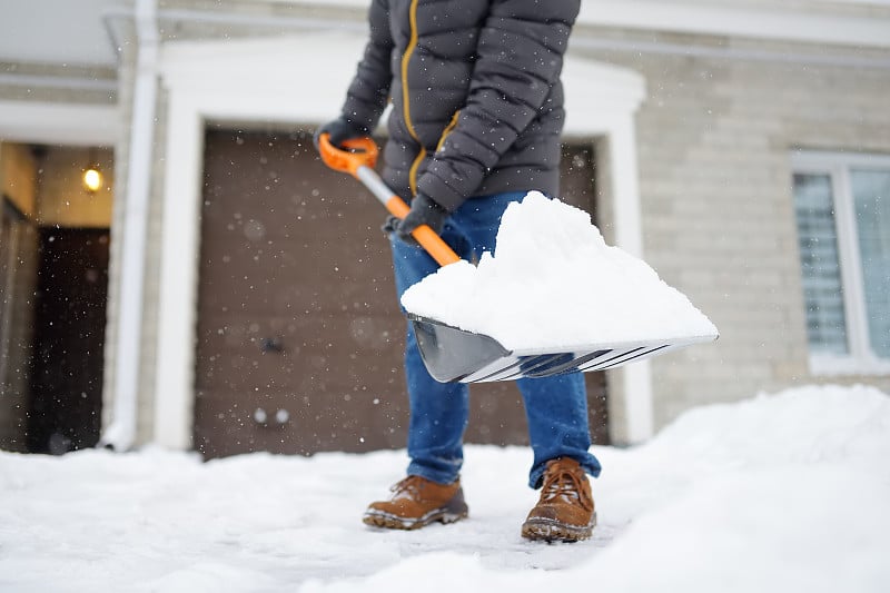 一名成熟的男子在暴风雪中清理房子附近的积雪。有人在铲车道上的雪。巨大的雪堆中。一场暴风雪过后，这个城