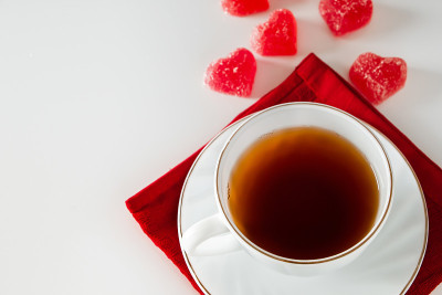 白色杯子，红餐巾上放着茶，还有心形的橘子酱