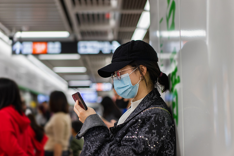 一位亚洲女士在地铁站等地铁时使用智能手机