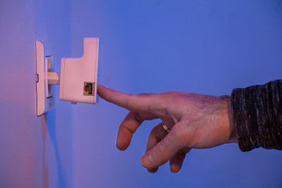 男人用手指按了一下WiFi中继器的按钮，它在墙上的电源插座上
