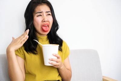 亚洲女人吃非常热和辣的面条从一个杯子她的嘴和舌头燃烧和红色