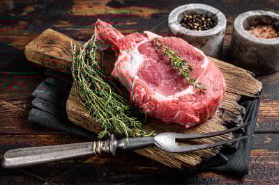 屠夫砧板上的生肋眼牛排或战斧牛肉(小牛肉)。木制背景。俯视图