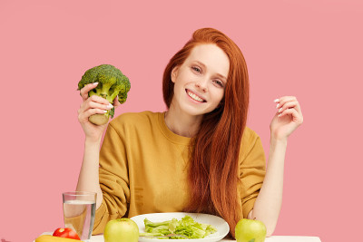漂亮的红发白人女人坐在桌前吃着健康的食物和西兰花