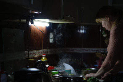 一个金发白种人女人晚上在家厨房里做饭，切洋葱。女人们在准备食物，闻着热气。的焦点