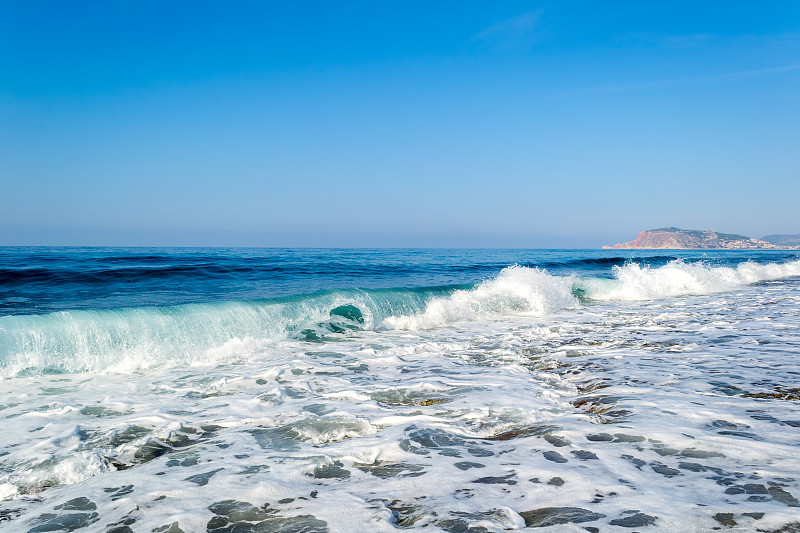 海浪冲击着多石的海滩，形成浪花