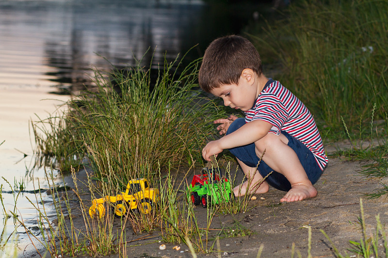 A little boy of 3 years plays on the river bank wi