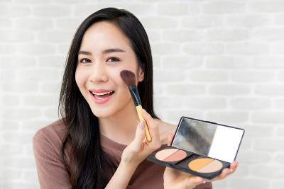 年轻美丽的微笑亚洲女人用腮红化妆