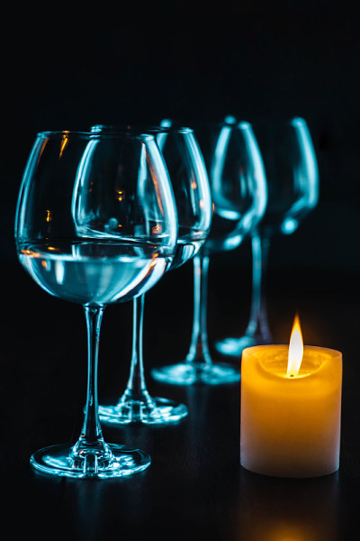 燃烧的蜡烛和黑色背景下的玻璃酒杯。餐桌上有明亮的蜡烛和雅致的酒杯。装有白葡萄酒的玻璃杯和蜡烛