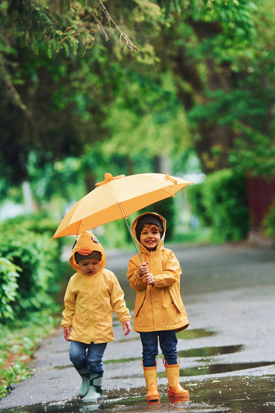 两个孩子打着雨伞，穿着黄色防水大衣和靴子，雨后一起在户外玩耍