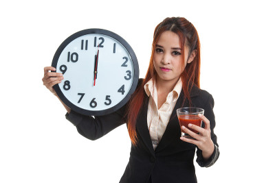 年轻的亚洲女商人拿着番茄汁和钟。