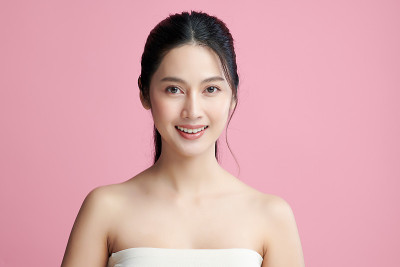 美丽年轻的亚洲女人与干净的新鲜皮肤在粉红色的背景，面部护理，面部治疗，美容和水疗中心，亚洲妇女肖像。