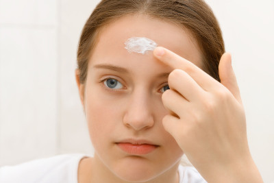 女孩把面霜涂在她的脸上，一个十几岁的女孩有着良好的皮肤，她看着镜子里的自己，美丽和健康的概念