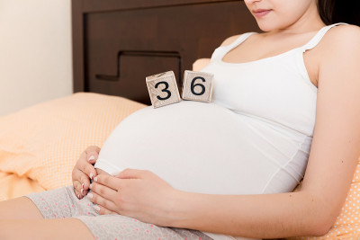 孕妇穿着白色内衣躺在家里的床上，手里拿着怀孕36周的日历。孕妇的概念。期待即将到来的孩子