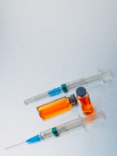 有选择性的重点。特写注射注射器和安瓿与橙色冠状病毒疫苗在银色铝背景。