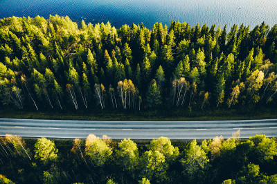 航拍的道路之间的绿色夏季森林和蓝色的湖在芬兰。