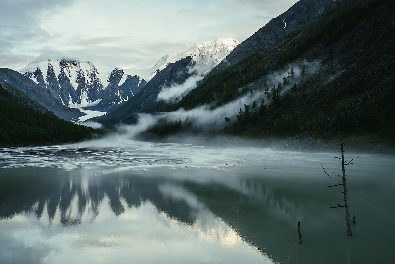 风景优美的高山景观与雪山在金色的阳光反射在低云雾山湖。大气高地风景与低云岩石和绿色镜湖。