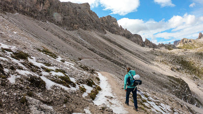 一名女子背着背包，拄着拐杖在意大利Dolomites的一条狭窄小路上徒步旅行。她周围有陡峭的山脉。很