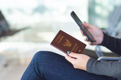 旅行的概念。特写的女人手持泰国护照和使用手机等待登机时间。