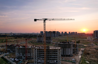 在日落的背景下，塔吊在施工现场活动。一台起重机在建造高层建筑。