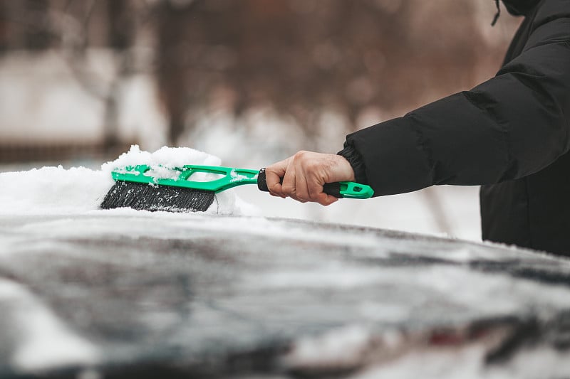 一个人用刷子清洗汽车上的结冰。暴风雪