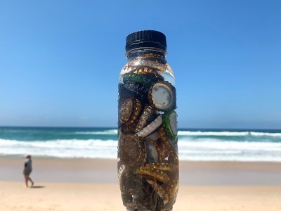 在一个阳光明媚的日子，在海滩上，被丢弃的啤酒瓶盖被收集在塑料饮料瓶中
