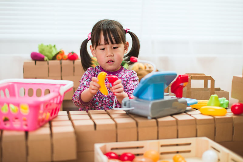 蹒跚学步的女孩在家里假装扮演甜蜜的店主