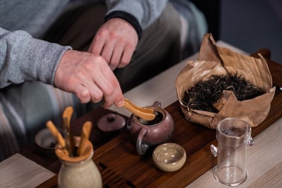 男子双手将特制的竹夹茶叶放入宜兴托盘制成的陶瓷茶壶中。制作中国茶的过程