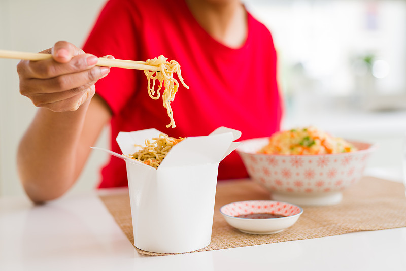 近距离的年轻女子吃面条从送盒使用筷子