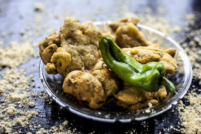 著名的Aloo pakora/ Aloo bhajia装在一个玻璃盘子里，上面撒有绿辣椒和鹰嘴豆粉。