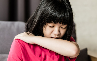 亚洲女童因空气污染过敏而咳嗽。亚洲小孩用肘部和手臂盖住嘴巴，以减少生病时咳嗽传播的病毒细菌数量