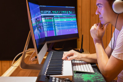 亚洲音乐制作人安排歌曲在MIDI键盘和桌面电脑在家庭工作室。音乐制作技术概念