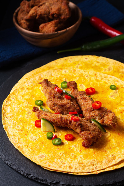食物概念辣炸鸡玉米饼卷与切碎的辣椒在黑色石板石背景与复制空间