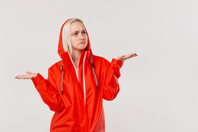 金发女孩穿着红色雨衣，带着兜帽表达愤怒的情绪，因为下雨的天气孤立在白色的背景。准备好迎接坏天气吧。
