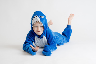 快乐的小男孩在白色背景上摆姿势，穿着睡衣kigurumi，蓝色鲨鱼服装