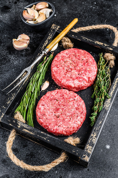 用碎肉和香草做成的生牛肉饼放在木板上。黑色背景。俯视图