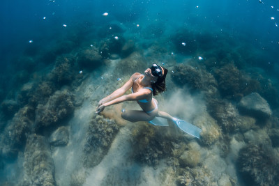 女自由潜水者在深海中滑行。自由潜水员与鳍摆姿势水下在蓝色的海洋
