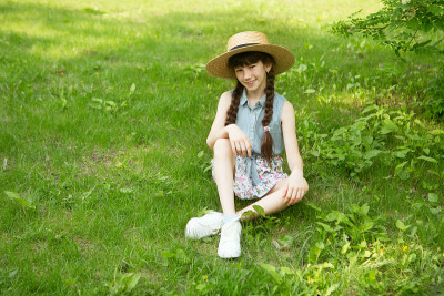 戴着帽子的小女孩微笑着坐在公园的绿草地上