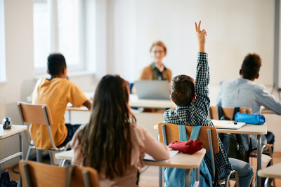 小学生在学校上课时举起手臂的背影。