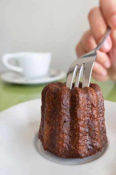 在巴黎的一家咖啡馆里，拿着叉子切着一个Canelé (Canele - Caneles de bor